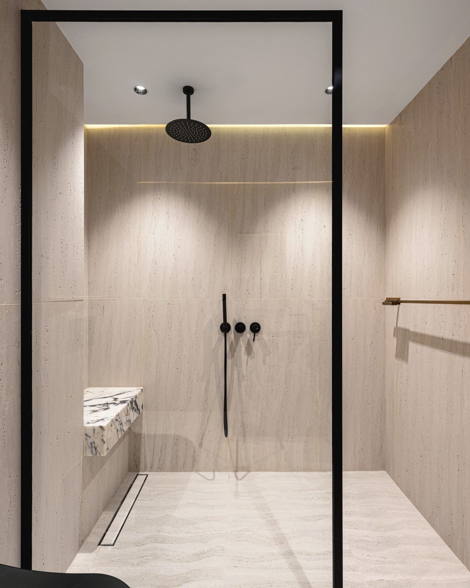 Minimal walk-in shower with a black glass frame and pale stone tiles